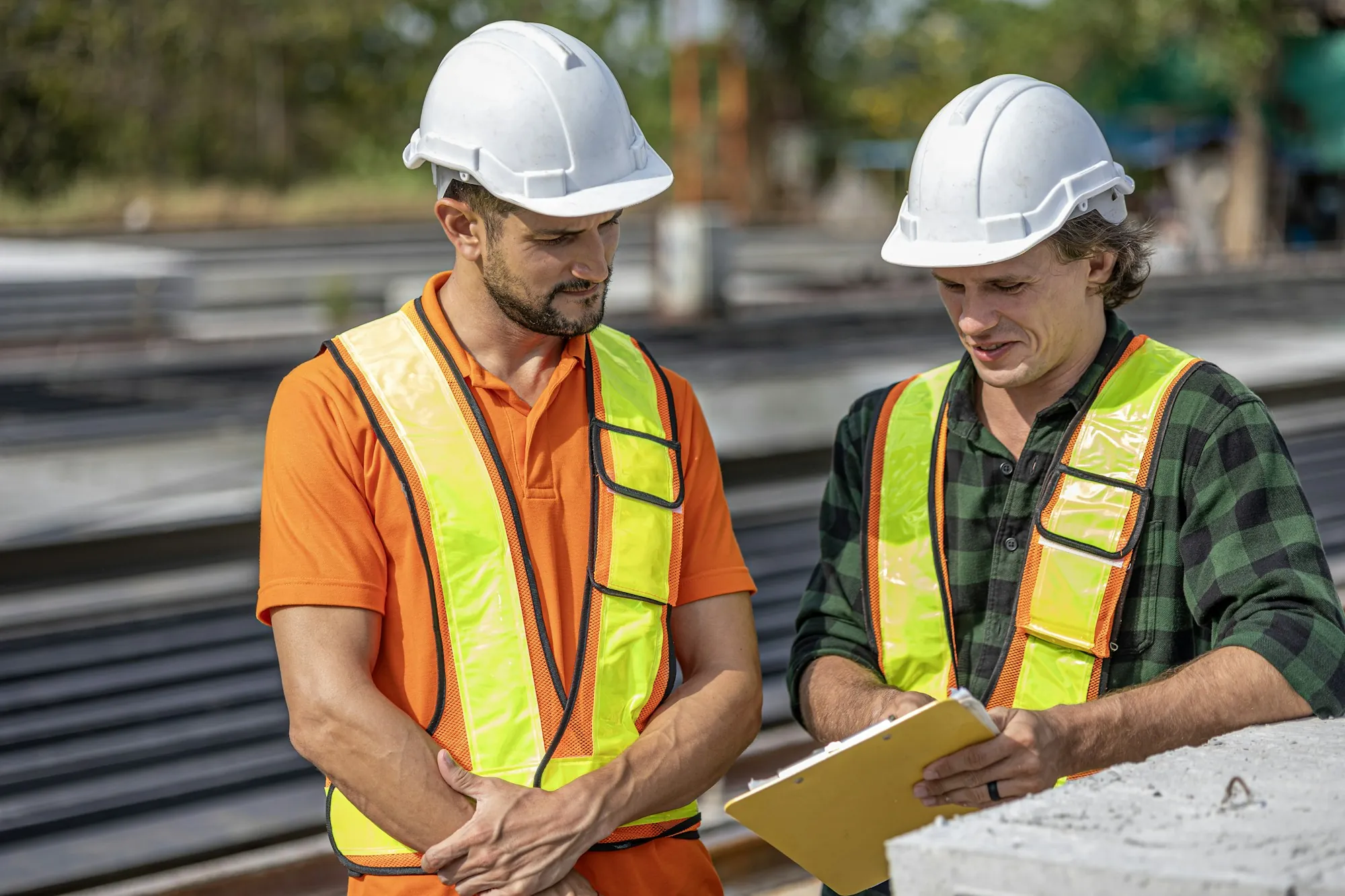 Two supervisors in hard hats reviewing a clipboard on site